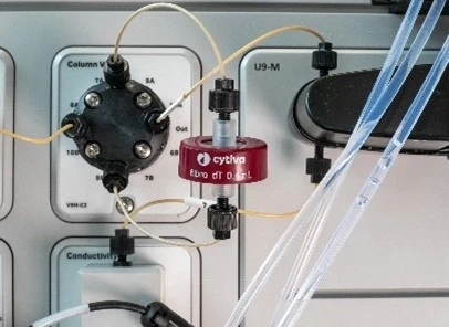 Close-up of a Cytiva fibro dT 0.1 L chromatography component connected to tubing and valves on a laboratory instrument panel, with visible labels for column valve and conductivity.