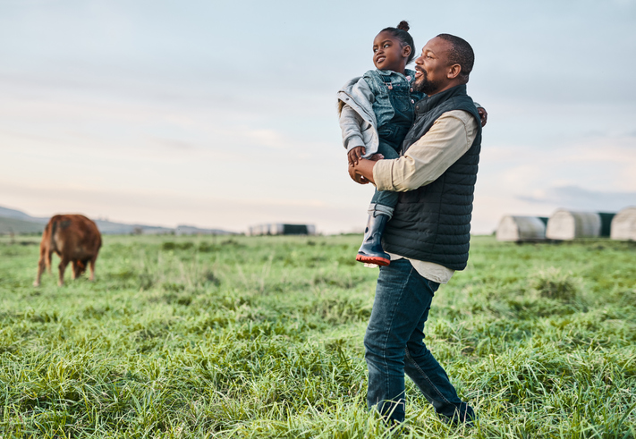 Man holding child on farm with horse grazing