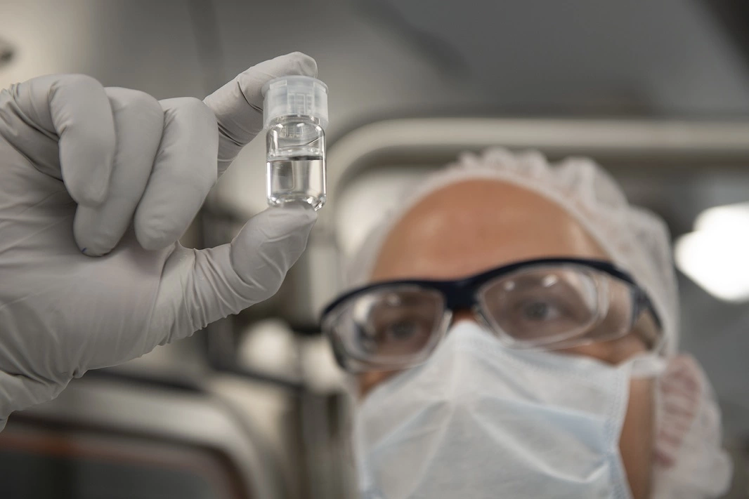 A cleanroom operator holds a filled and capped pharmaceutical vial