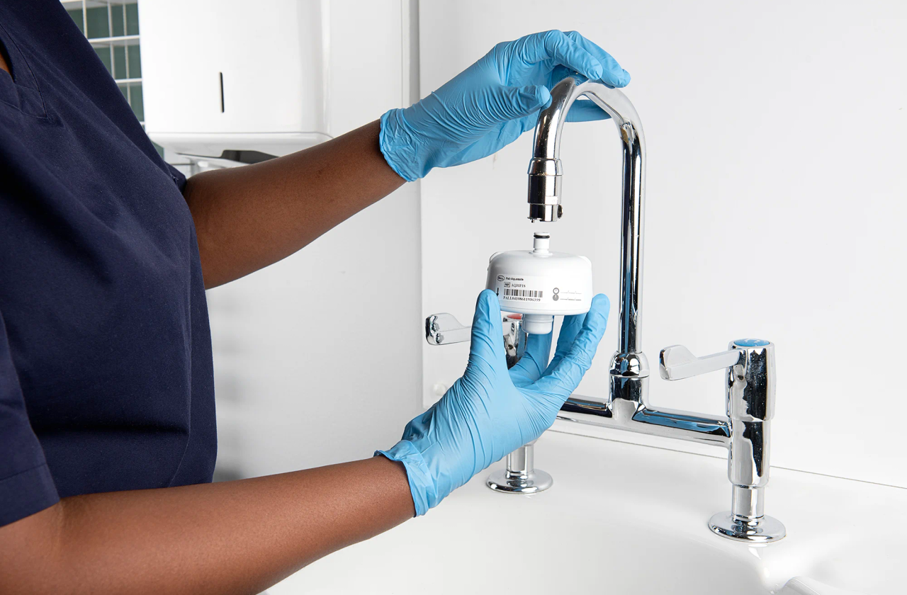 Healthcare staff member using a faucet with an installed Pall Aquasafe filter.