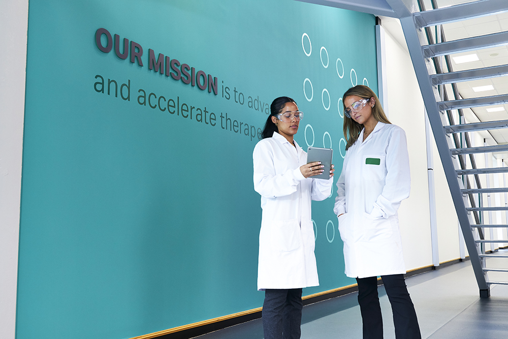 Scientists discussing in corridor with Cytiva brand mission statement on the wall, action shot 2 (low res)