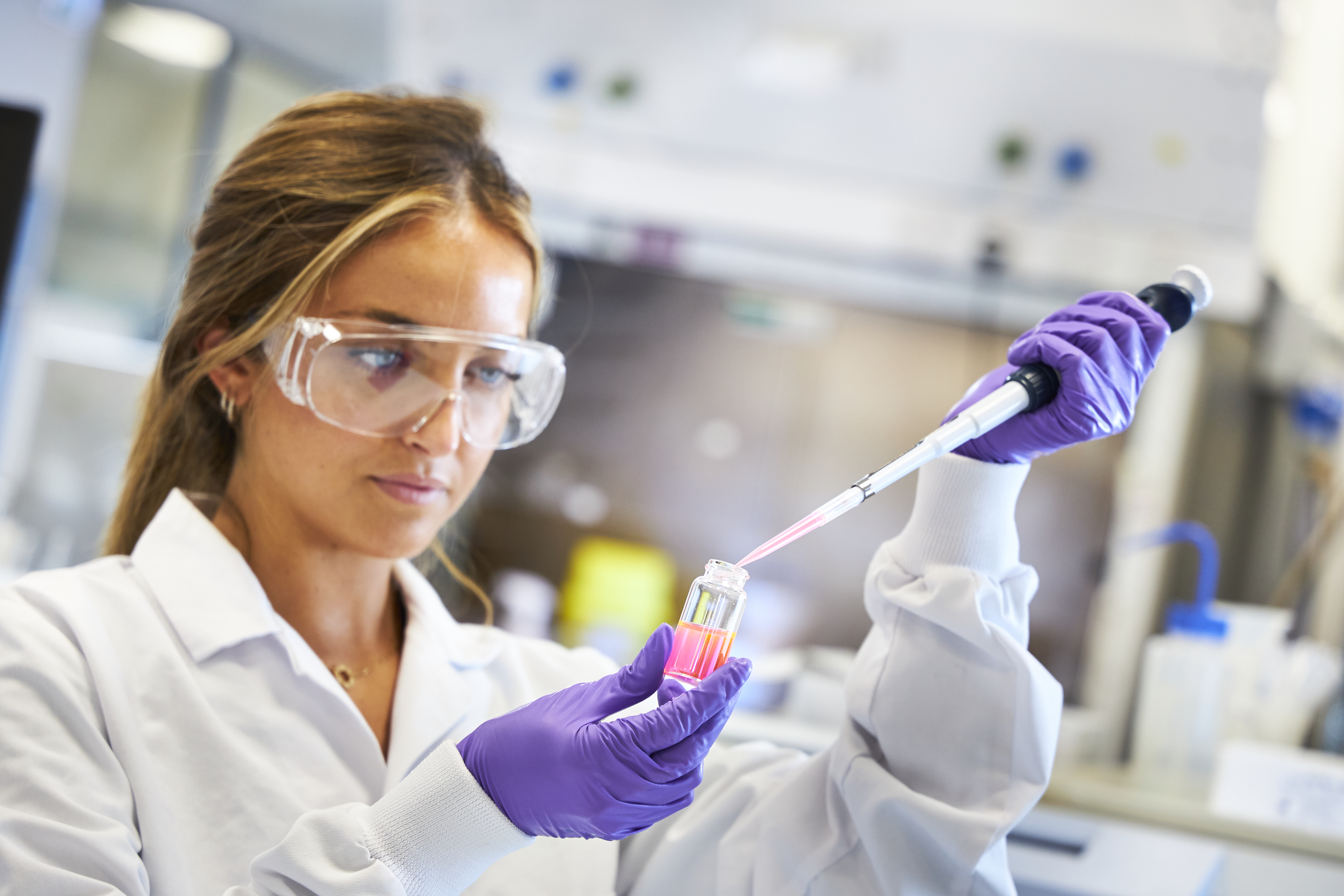 Close up of scientist using a pipette at lab bench, mask off, looking down, close up, side view (high res)